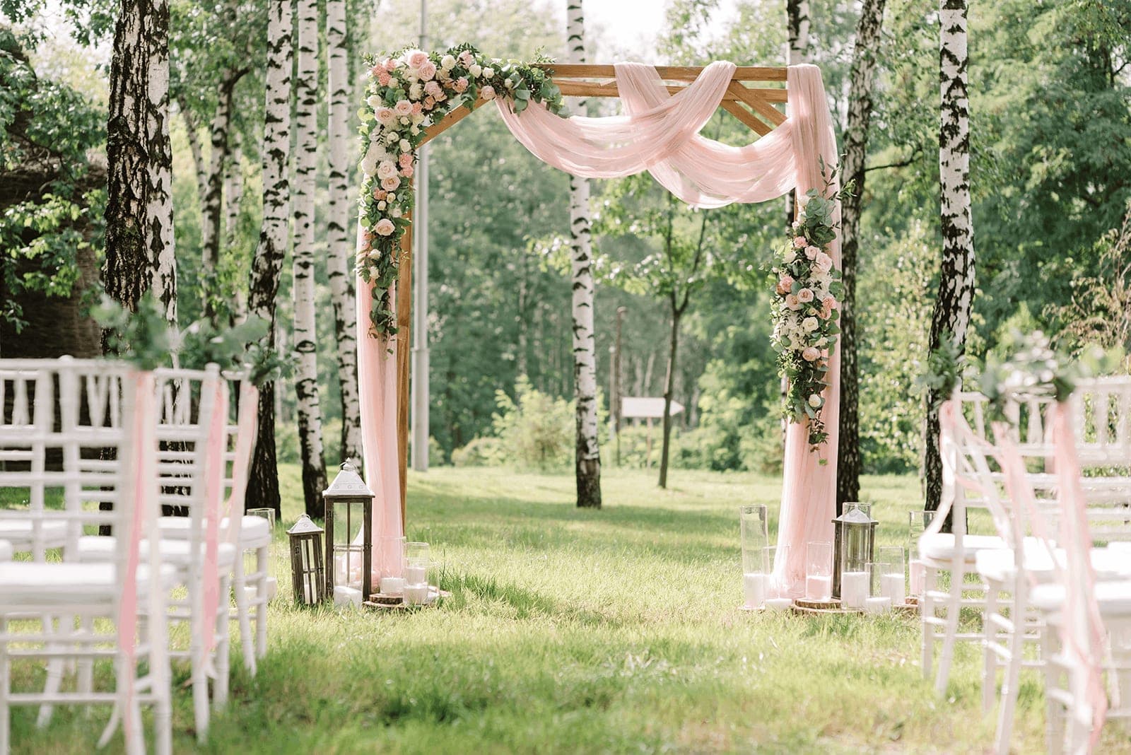 A garden ceremony with pink drapes over a wooden arch and white chairs on the lawn