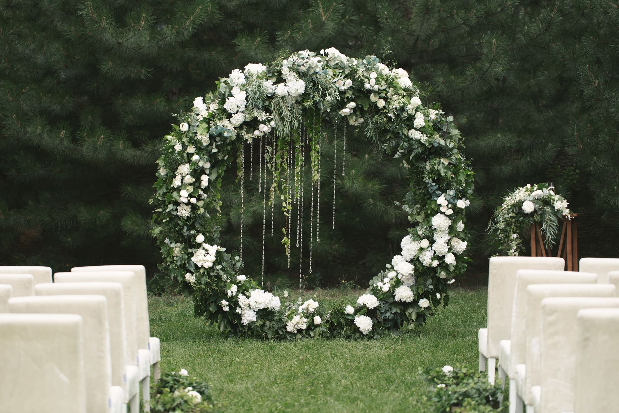 A floral ceremony arch facing rows of white chairs on a garden lawn